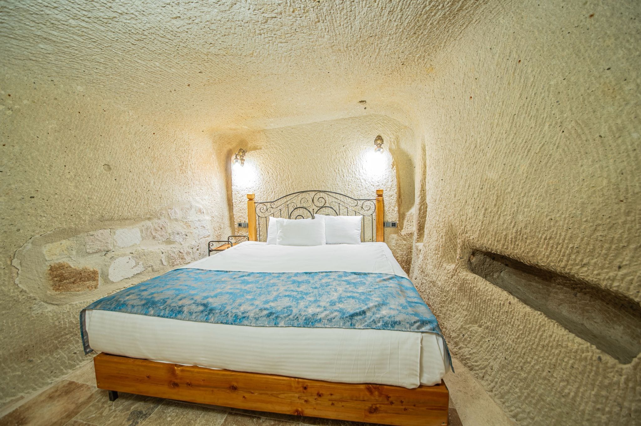 Ein Schlafzimmer mit einem hölzernen Bett, weißer Bettwäsche und einer Wand aus strukturiertem Stein.