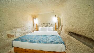 Ein Schlafzimmer mit einem hölzernen Bett, weißer Bettwäsche und einer Wand aus strukturiertem Stein.