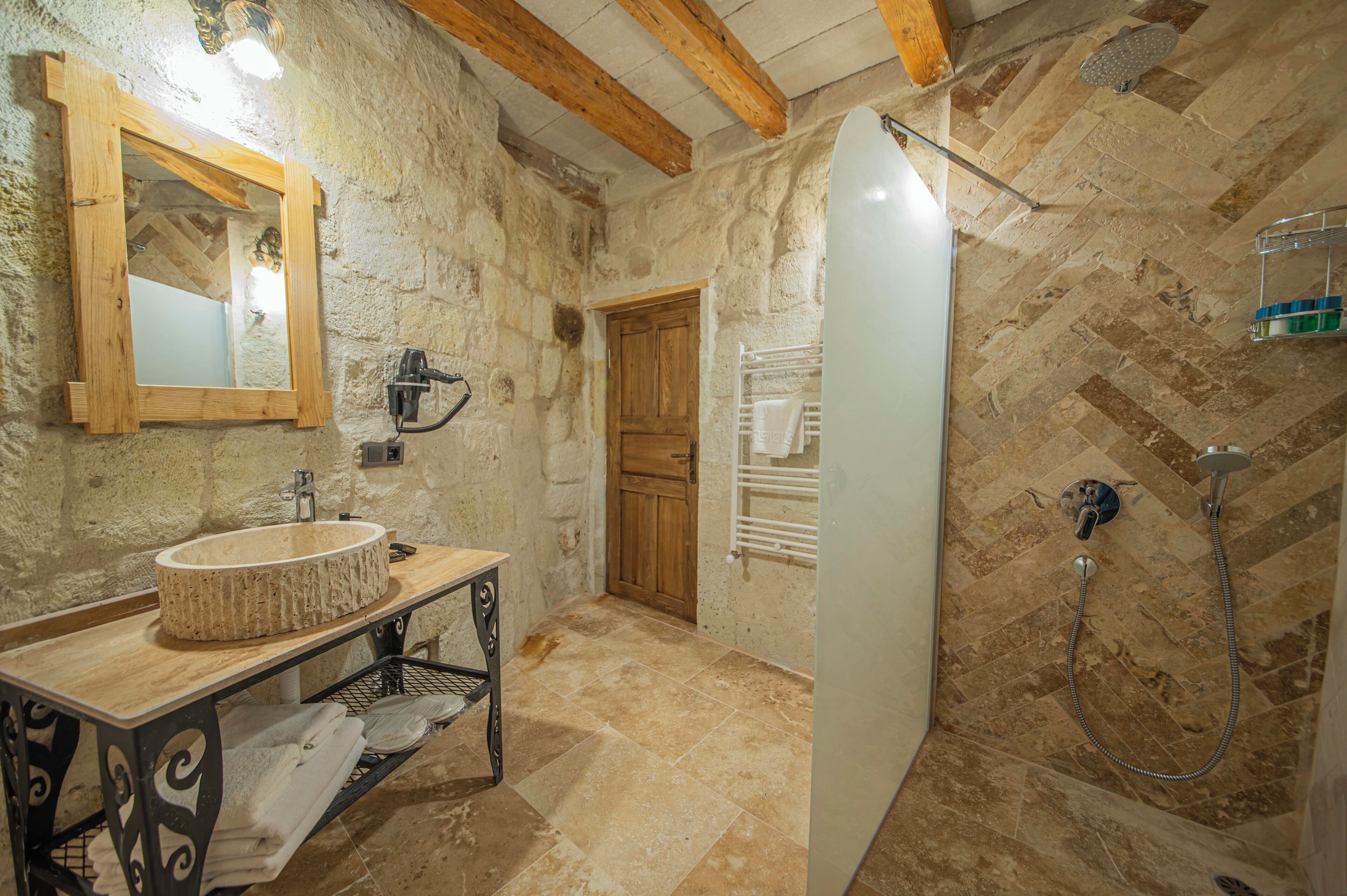 A stone-walled bathroom with a wooden vanity, a mirror, a shower with a handheld showerhead, and a towel rack.