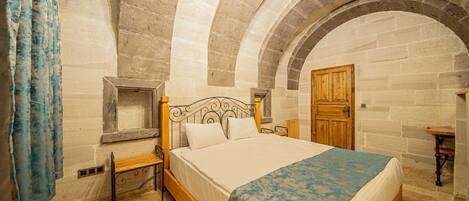 A bedroom with a bed, wooden headboard, stone walls, and an arched ceiling.