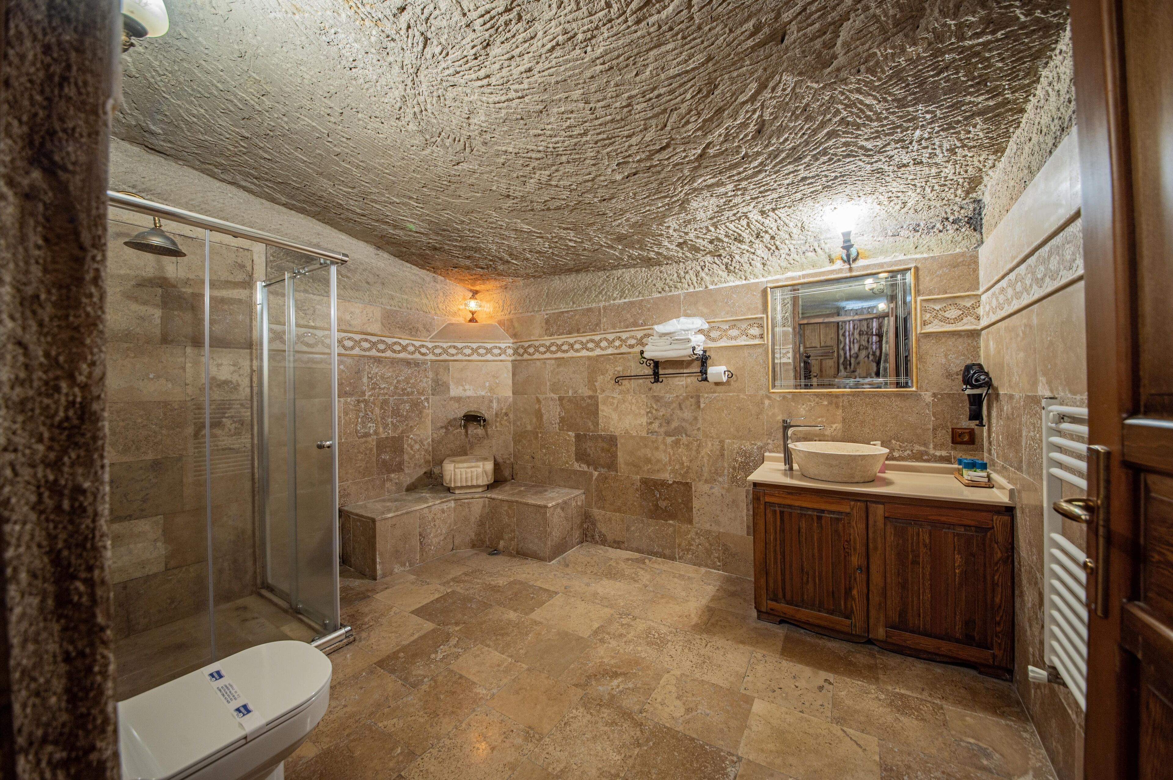 A bathroom with a shower, toilet, sink, and wooden cabinets.