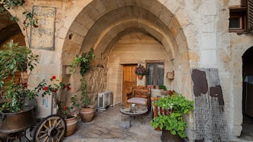 Ein Innenhof mit Steinbögen, Blumentöpfen, einem Holzstuhl und einem alten Ventilator.