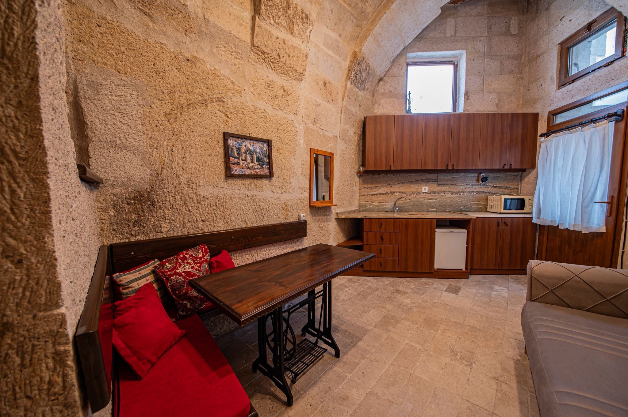 Una habitación rústica con paredes de piedra, un banco de madera, una mesita y una pequeña cocina.