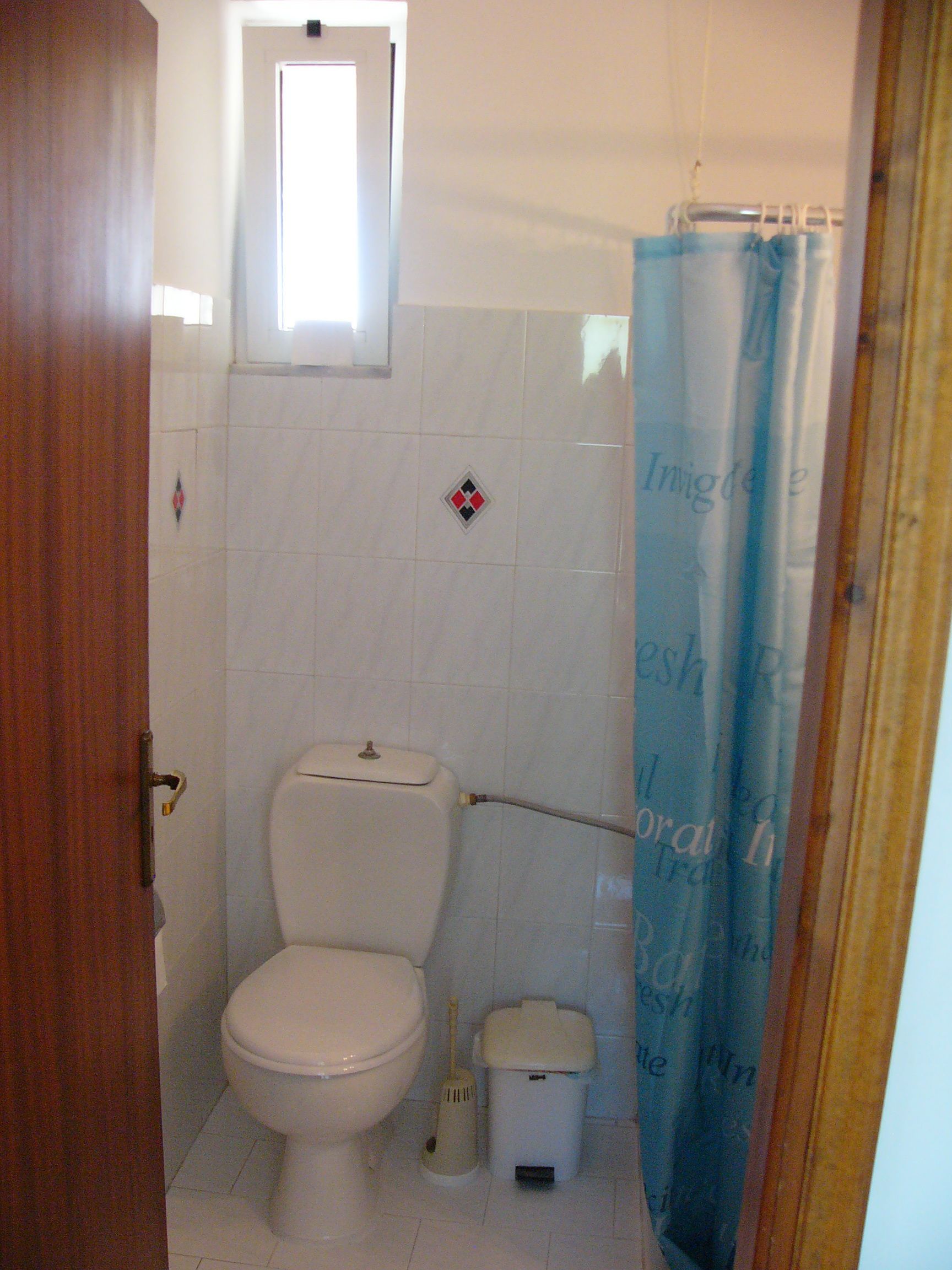 Une petite salle de bain avec des toilettes, une poubelle et un rideau de douche.