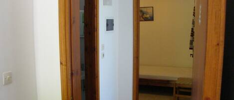 A narrow hallway with a wooden door leading to a room with a bed and a small table.