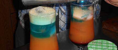 Two cocktails in tall glasses with layered colors, a metal shaker, and a spoon.