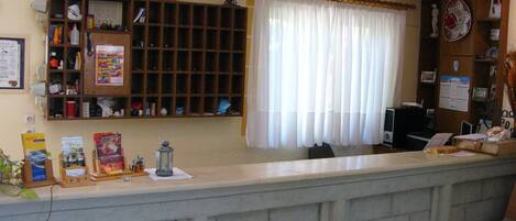 A reception area with a counter, a bulletin board, and a window with sheer curtains.