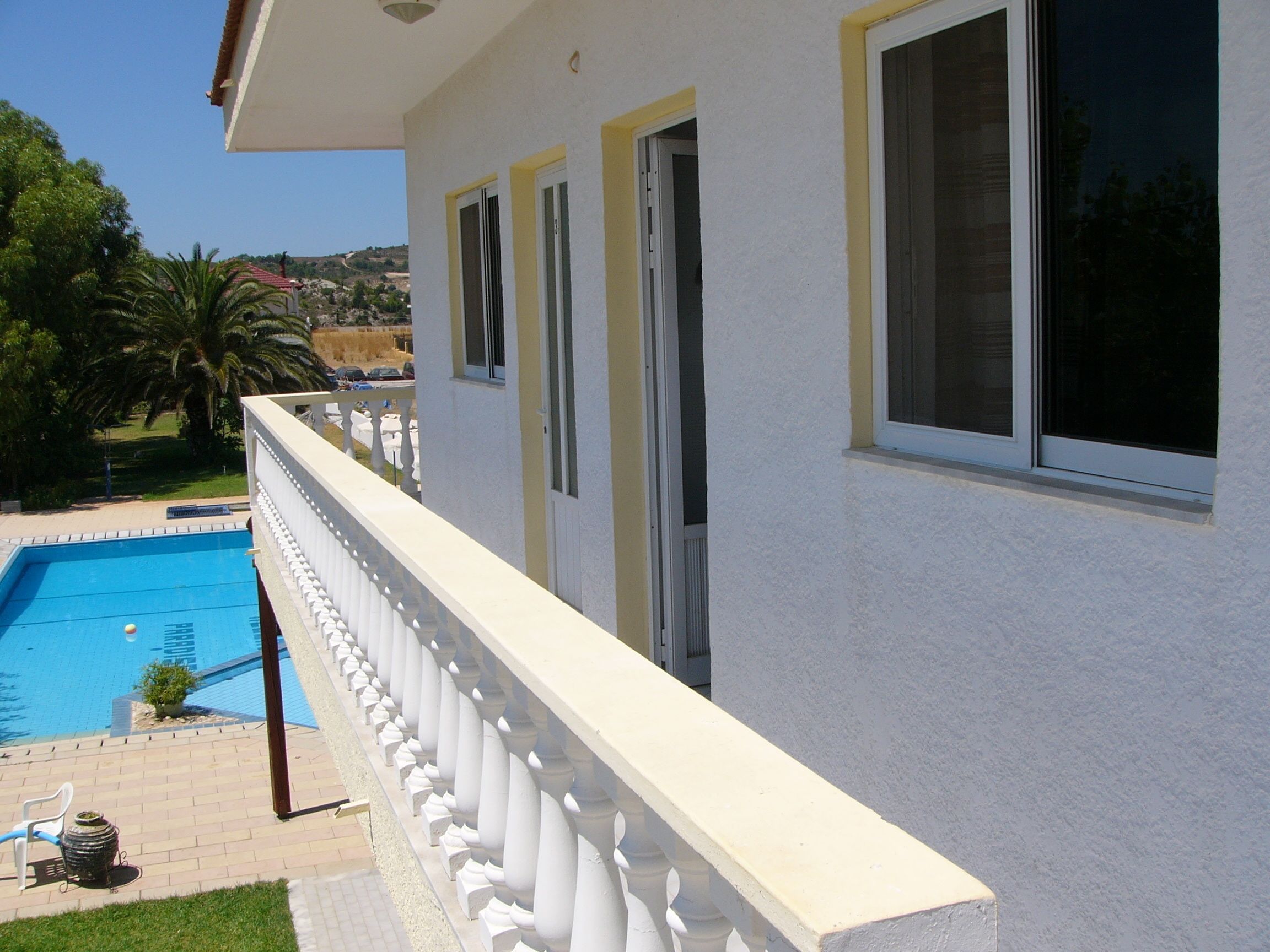 Un edificio con piscina, un balcón con barandilla blanca y vistas del paisaje circundante.