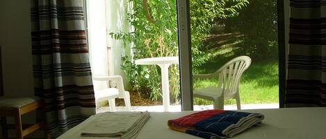 Una habitación con una cama, una mesita y una silla. Se ve vegetación por la ventana.