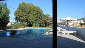Una piscina con solárium empedrado, rodeada de árboles y un cielo azul despejado.