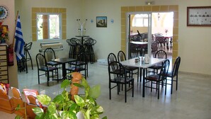 Un comedor con varias mesas y sillas, un ventilador de techo y una ventana con cortinas.