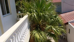 Un balcón con barandilla blanca, una palmera y suelo de baldosas.