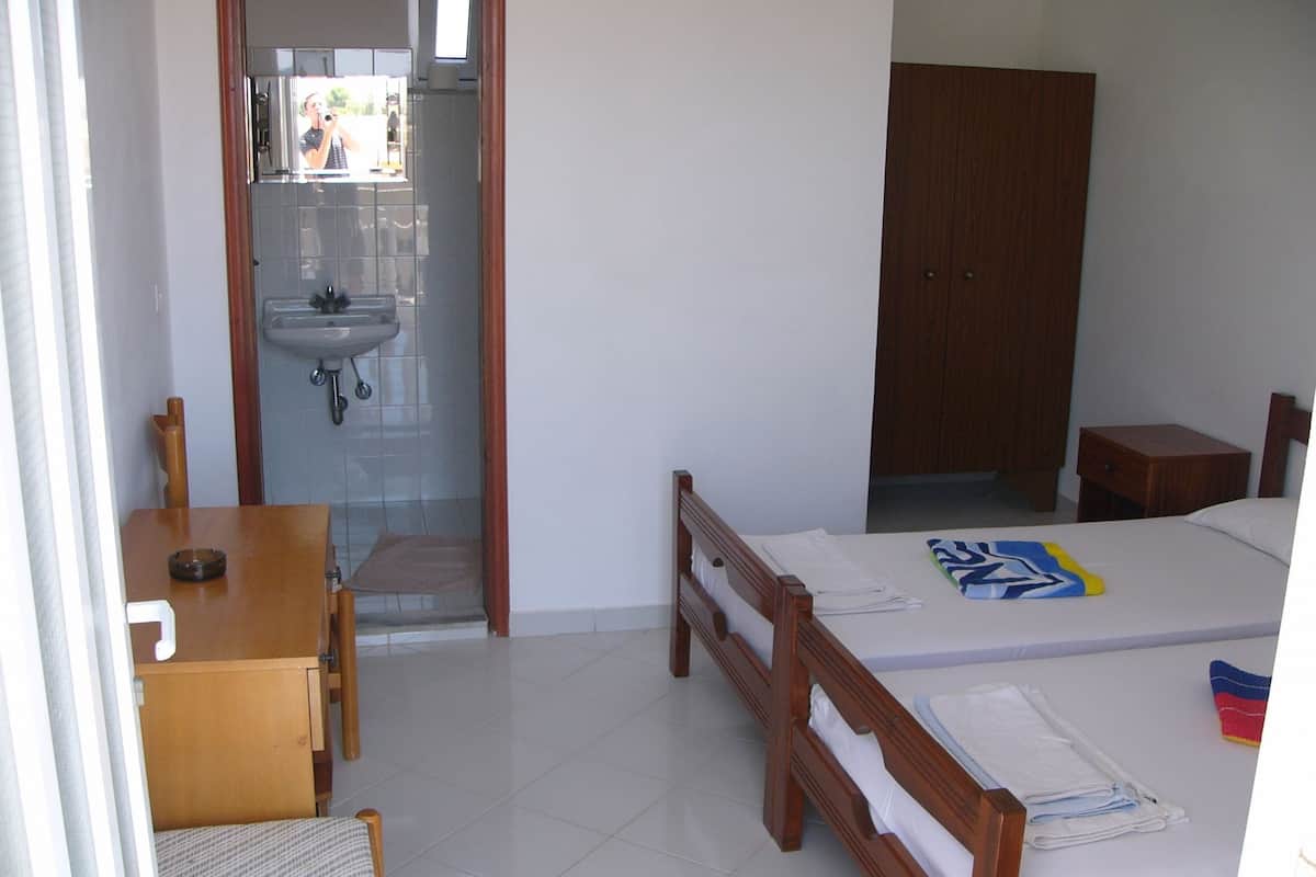 A hotel room with a bed, a wooden desk, a chair, a wardrobe, and a bathroom with a sink and mirror.