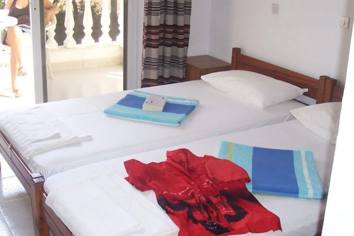 A room with two beds, each with white linens and a blue and white striped towel.