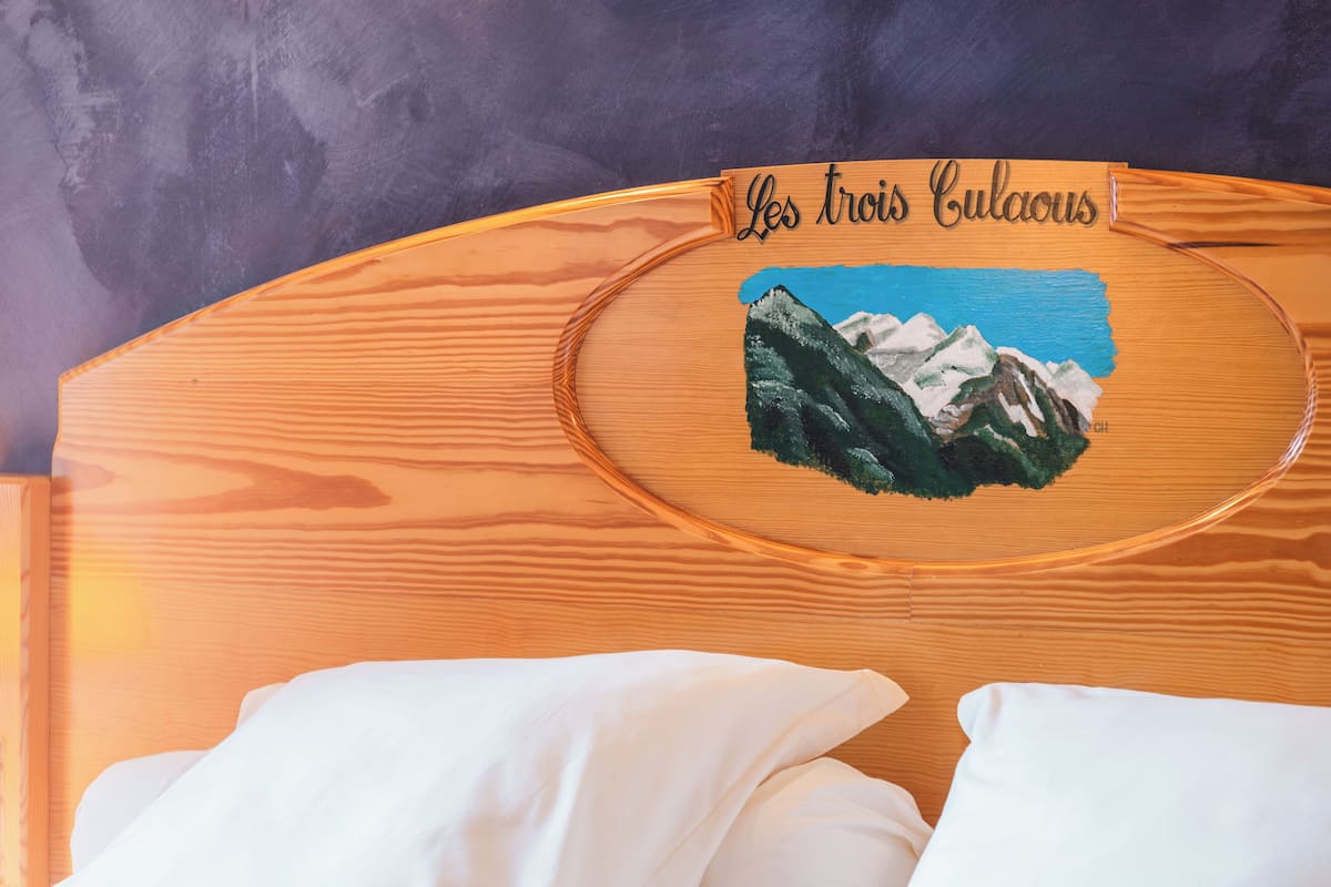 Une tête de lit en bois ornée d’un tableau représentant des montagnes et portant l’inscription « Les trois Culautus ».