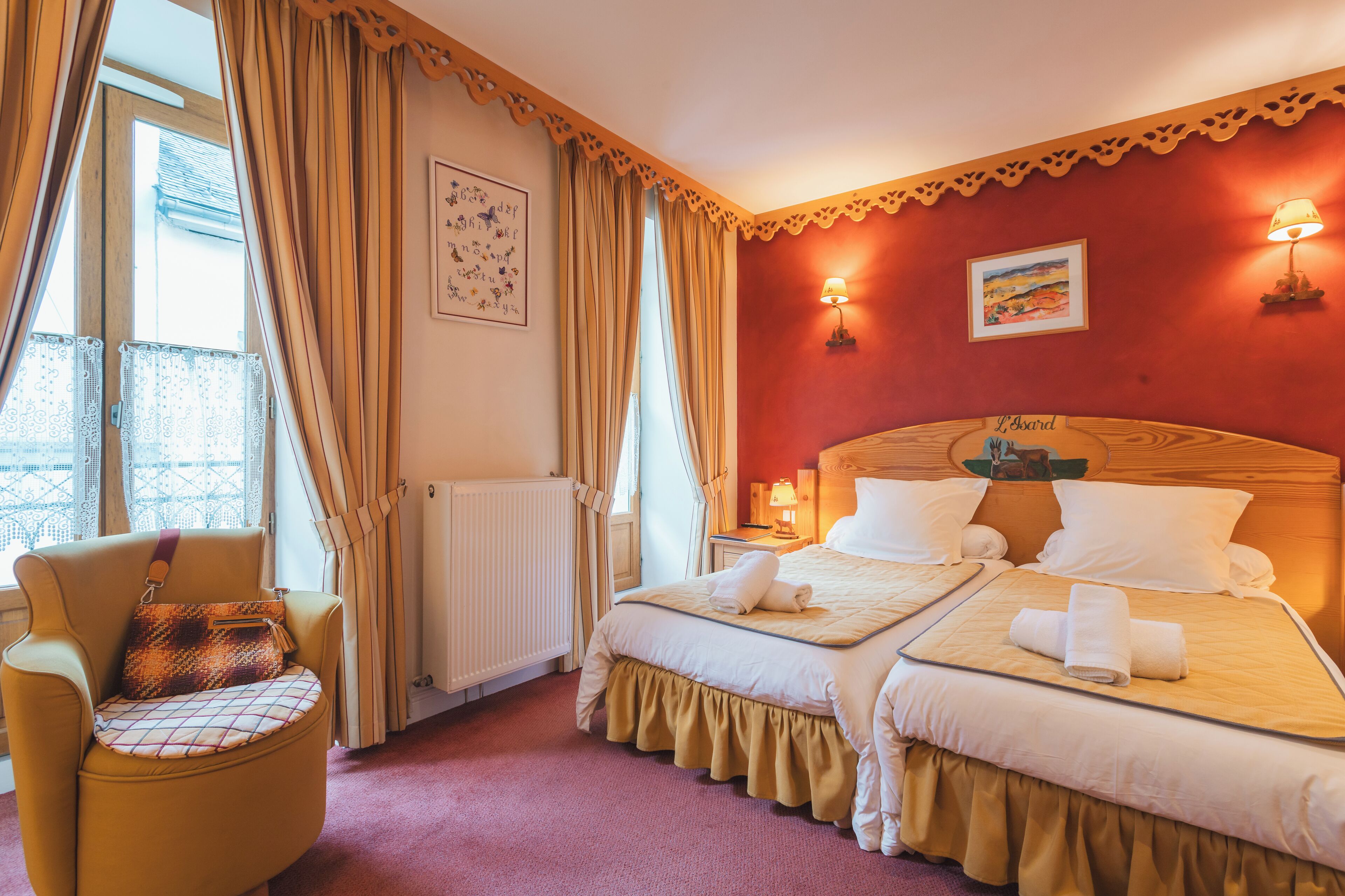 Une chambre d’hôtel avec deux lits, une chaise dotée d’un coussin à motifs, un radiateur et une fenêtre avec des rideaux.