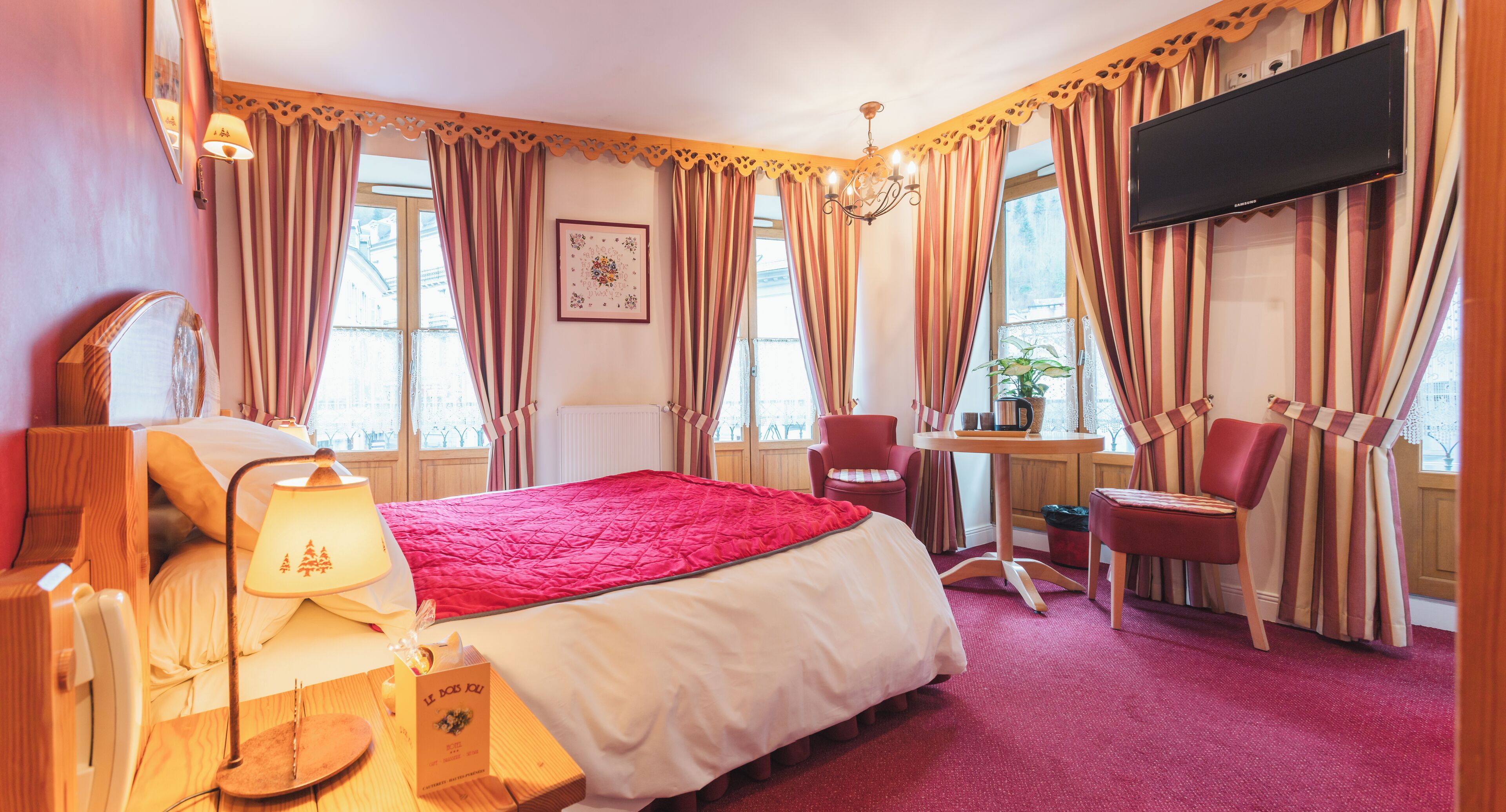 Habitación de hotel con una cama grande, un escritorio con silla, televisión y ventana con cortinas.