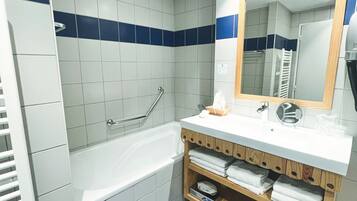 Un baño con bañera, lavamanos con espejo y estante con toallas.