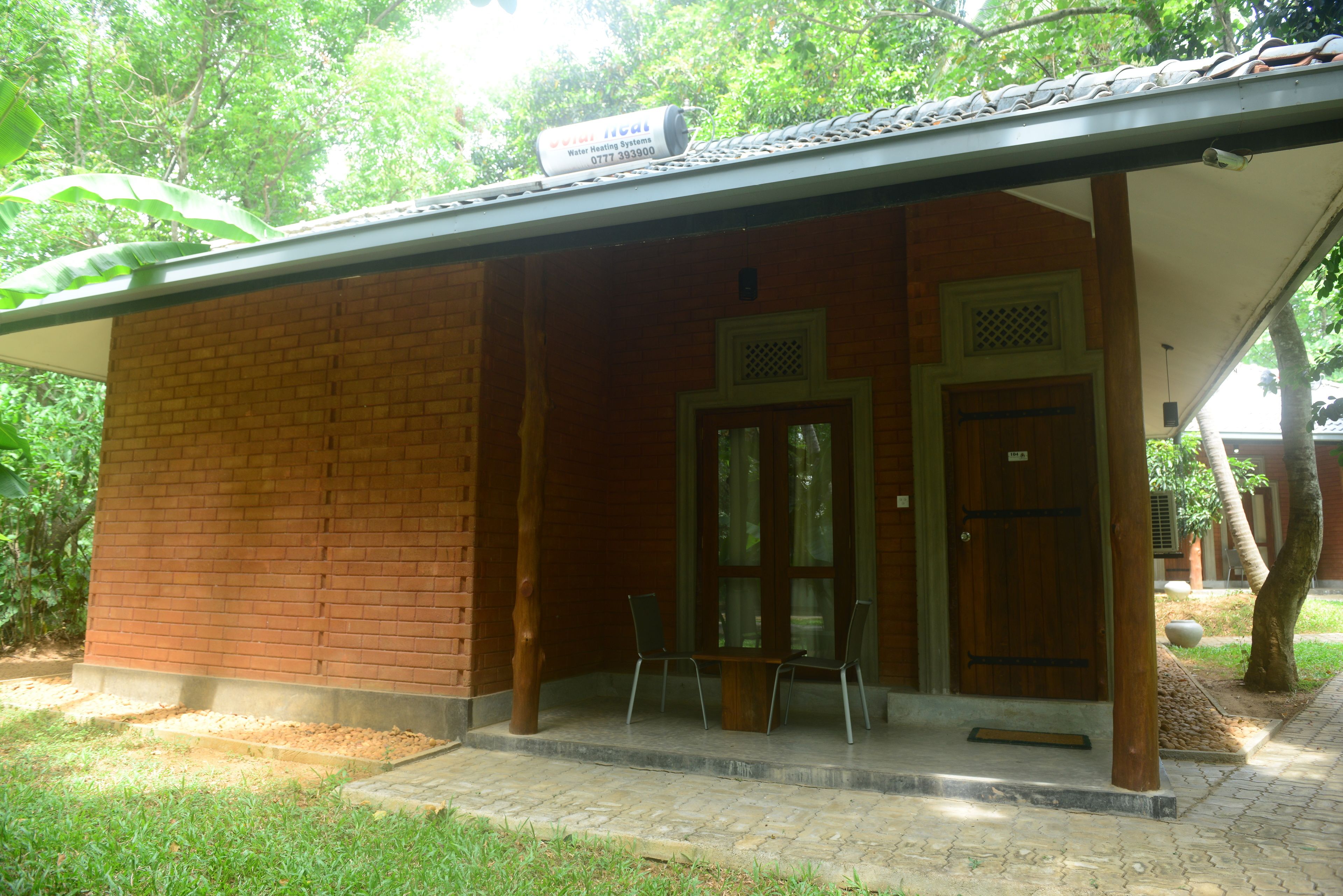 A small brick building with a covered porch, two doors, and a sign indicating a water heating system.