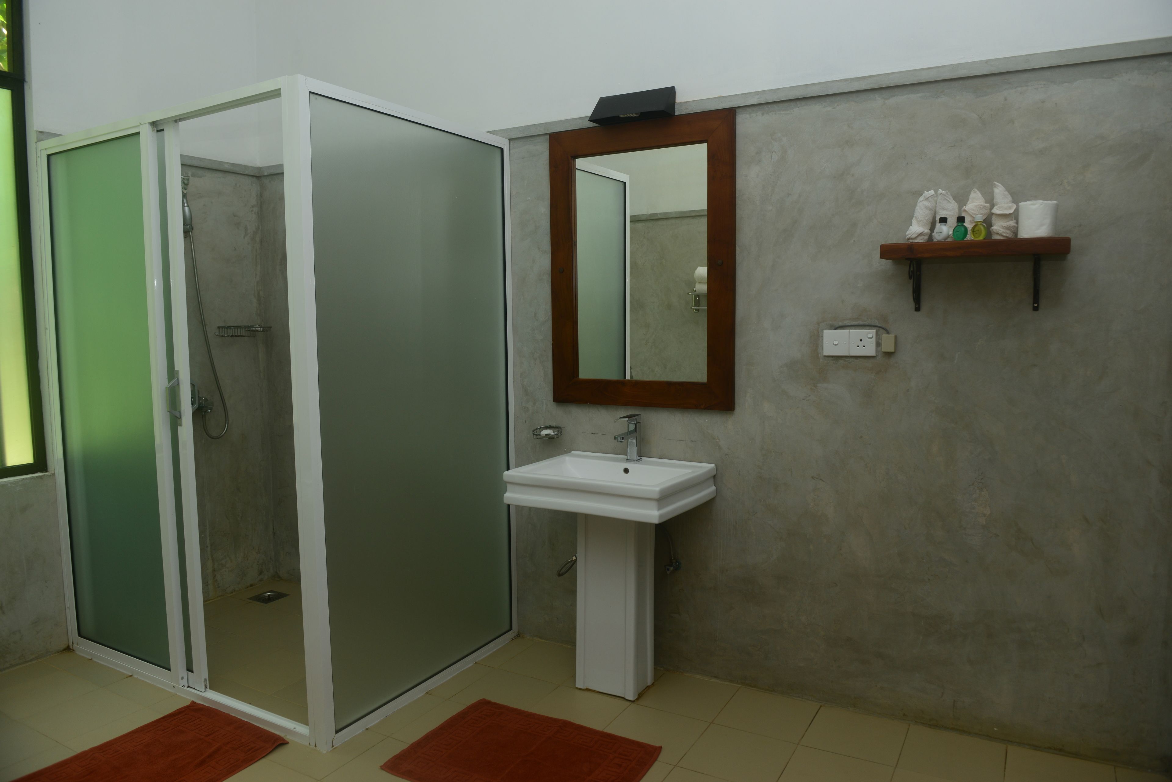 Ein Badezimmer mit einer gläsernen Duschkabine, einem weißen Waschbecken, einem Spiegel und einem Ablagebereich für Toilettenartikel.