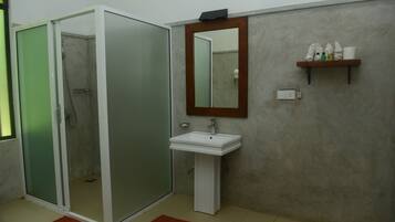 Ein Badezimmer mit einer gläsernen Duschkabine, einem weißen Waschbecken, einem Spiegel und einem Ablagebereich für Toilettenartikel.