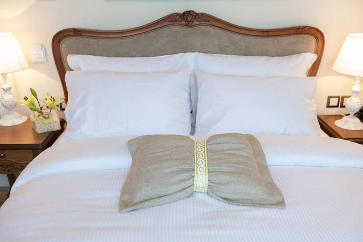 Una cama bien tendida con una toalla doblada en el centro, un cabecero de madera y dos lámparas de noche.