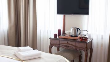A hotel room with a bed, a bedside table with a coffee maker, a TV, and curtains.