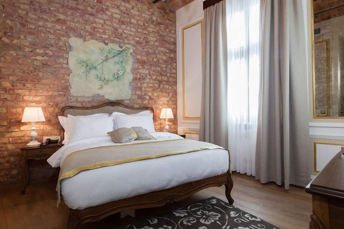 Un dormitorio con pared de ladrillo, una cama con ropa de cama blanca, dos lámparas de noche y un ventanal con cortinas.