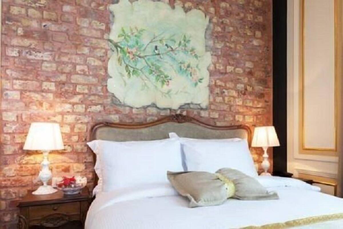 Une chambre d’hôtel avec un mur en briques, un lit recouvert de draps blancs, deux lampes de chevet et un tableau décoratif au-dessus du lit.