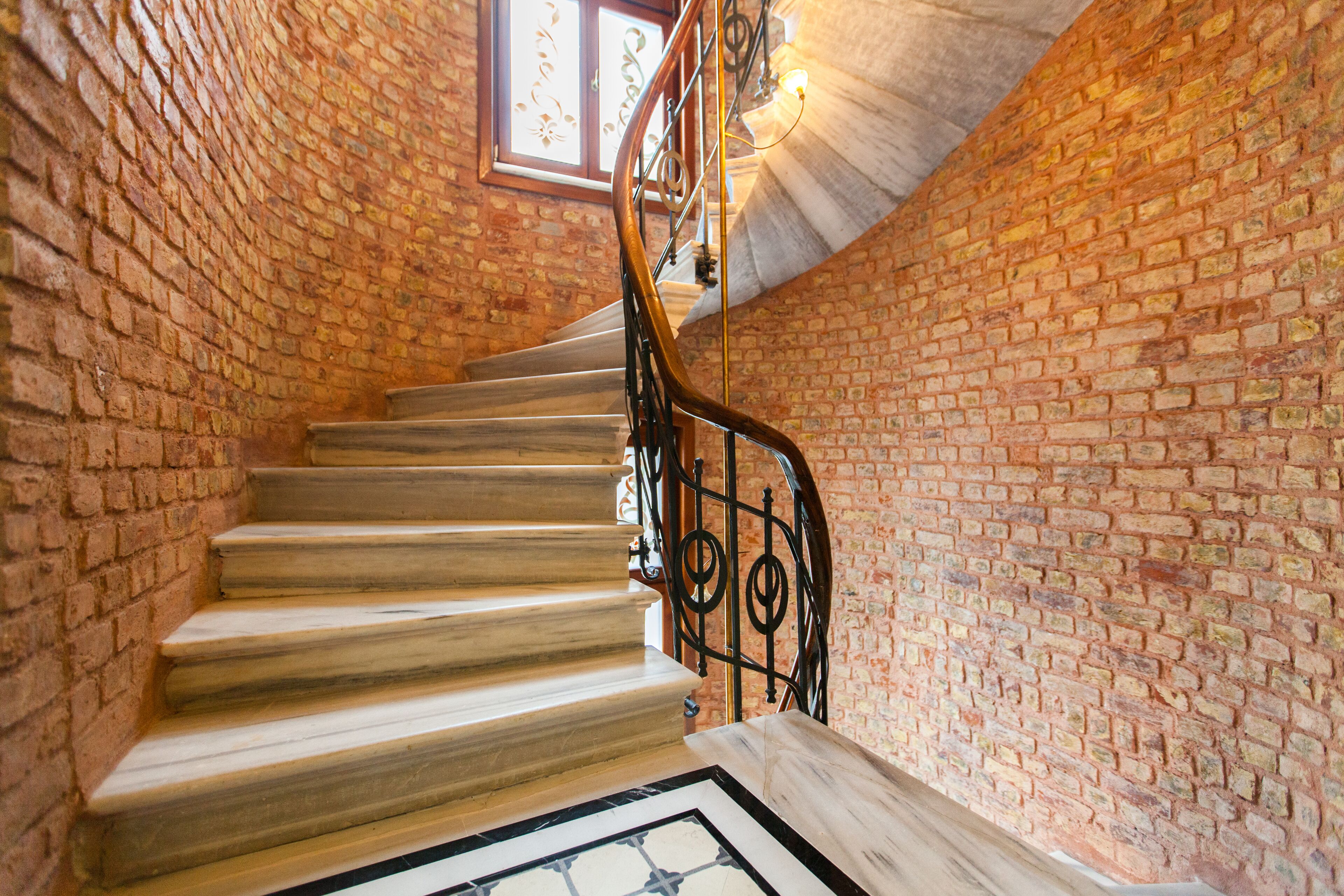 A spiral staircase with wooden steps and black metal railings, surrounded by brick walls.