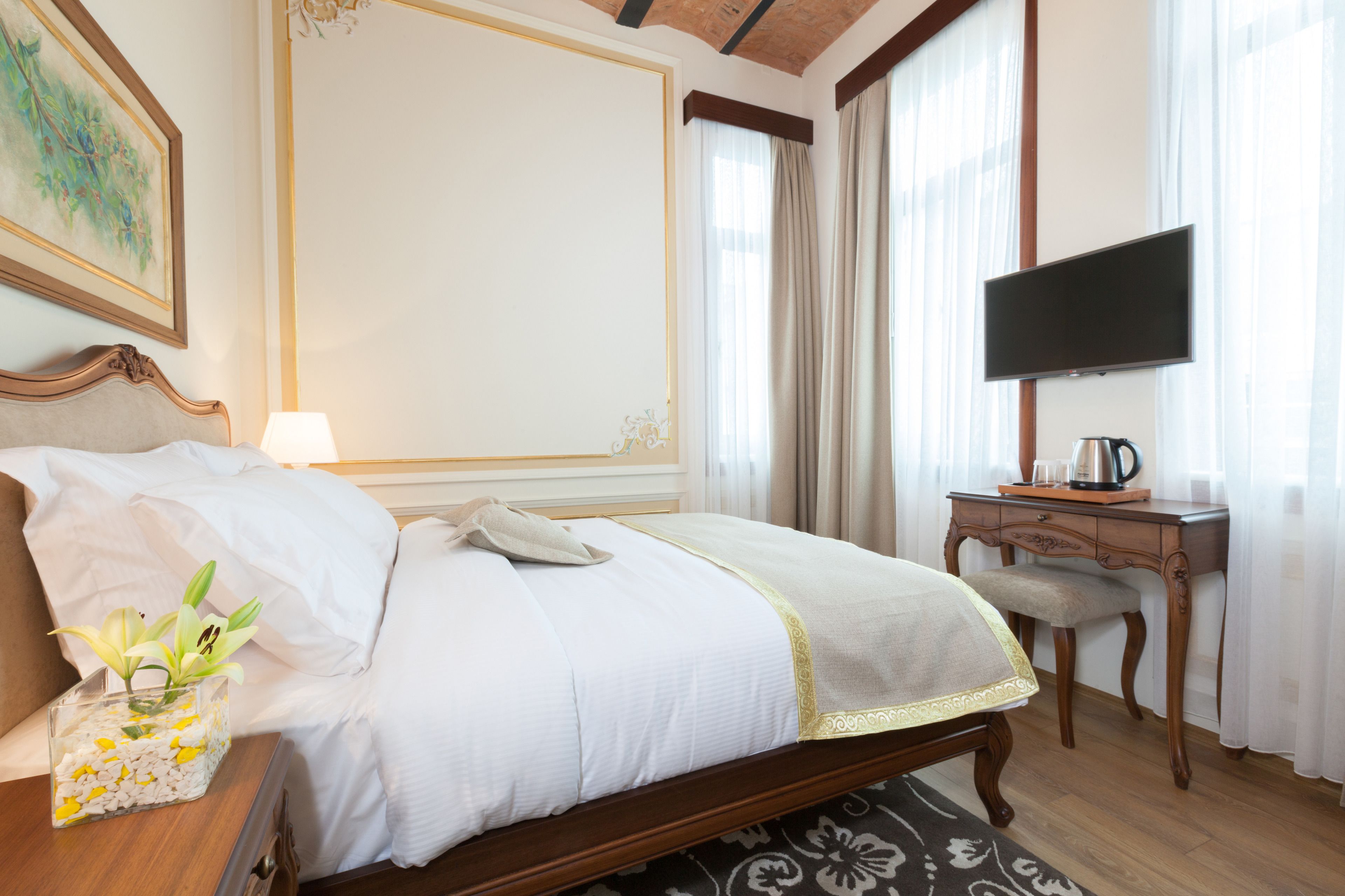 Habitación de hotel con una cama grande, un escritorio con televisor de pantalla plana, una cafetera y un florero con flores en la mesita de noche.