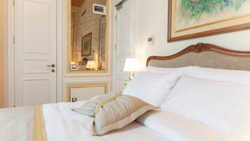 A neatly made bed with white linens and two pillows, a wooden headboard, a nightstand with a lamp, and a framed painting on the wall.