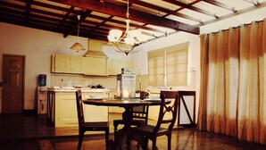 A dining area with a wooden table and chairs, a chandelier, and a kitchen in the background. - City Hub Lagoon (Negombo)