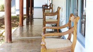 A covered outdoor area with wooden chairs and a bench, wooden pillars, and a white building with blue trim. - City Hub Lagoon (Negombo)