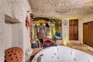 Una habitación con pared de piedra, puerta de madera, una bañera, una pequeña mesa y un banco.
