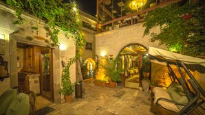 Un patio con suelo de piedra, plantas en macetas, una silla colgante y un restaurante con terraza.