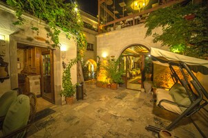 A courtyard with stone flooring, potted plants, a swing chair, and a restaurant with outdoor seating.