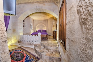 A narrow passageway leading to a room with a bed, a wooden door, and a patterned rug. - Hidden Cave (Nevsehir)