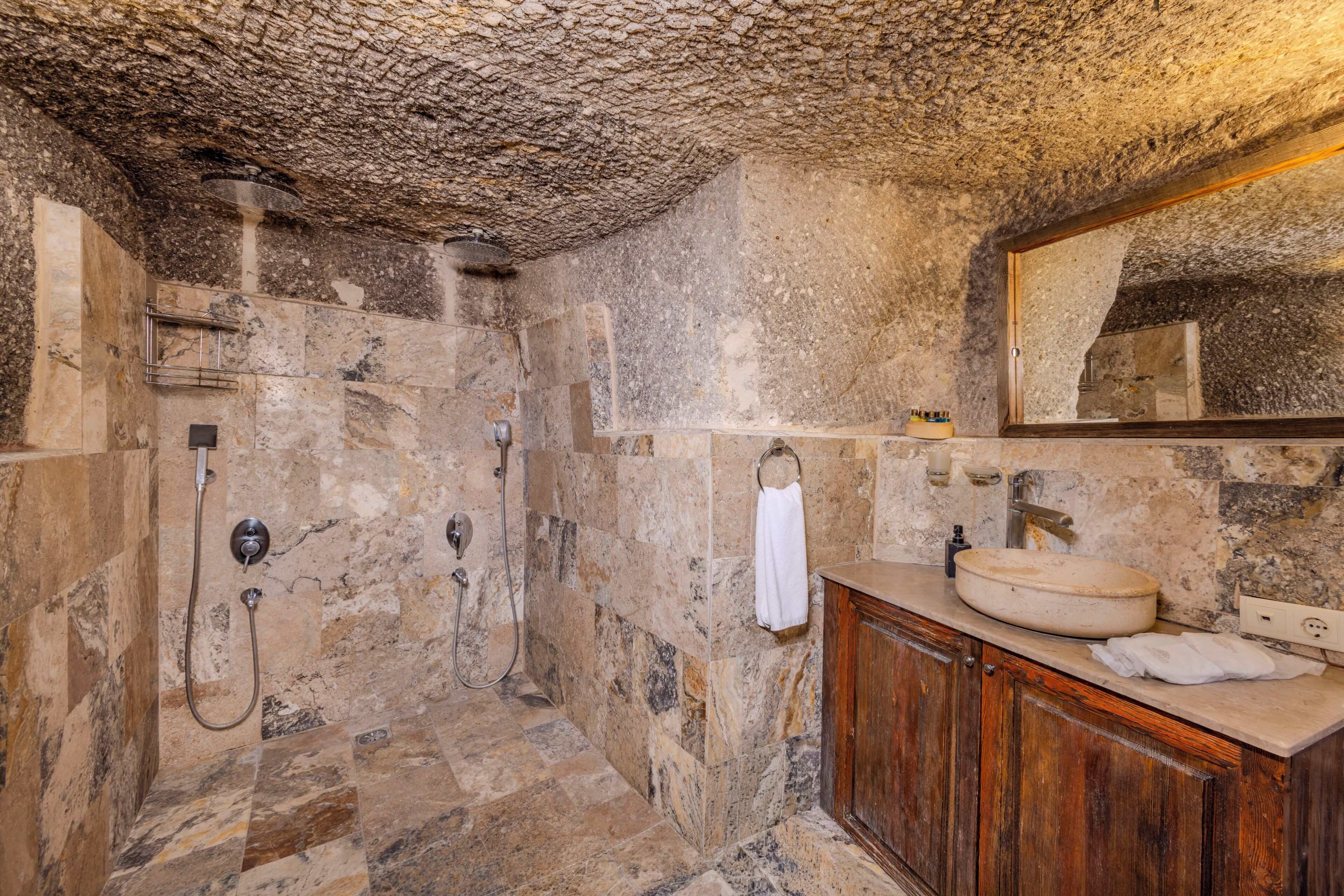 A stone-walled bathroom with a wooden vanity, a round sink, and a shower with multiple fixtures.