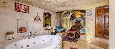 A bathroom with a large bathtub, a mirror, and a wooden door.