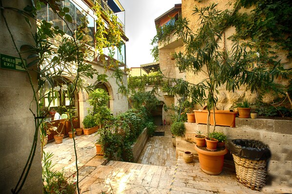 Un patio estrecho con plantas en macetas, un muro de piedra y un contenedor de basura.