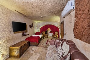A room with a bed, a television, a red curtain, and a fireplace. - Hidden Cave (Nevsehir)