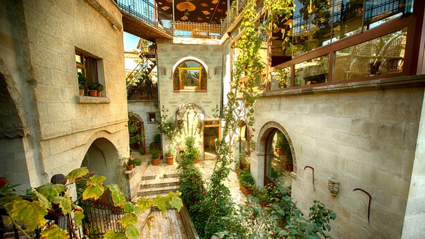 Un patio con paredes de piedra, puertas con arcos y plantas en macetas.