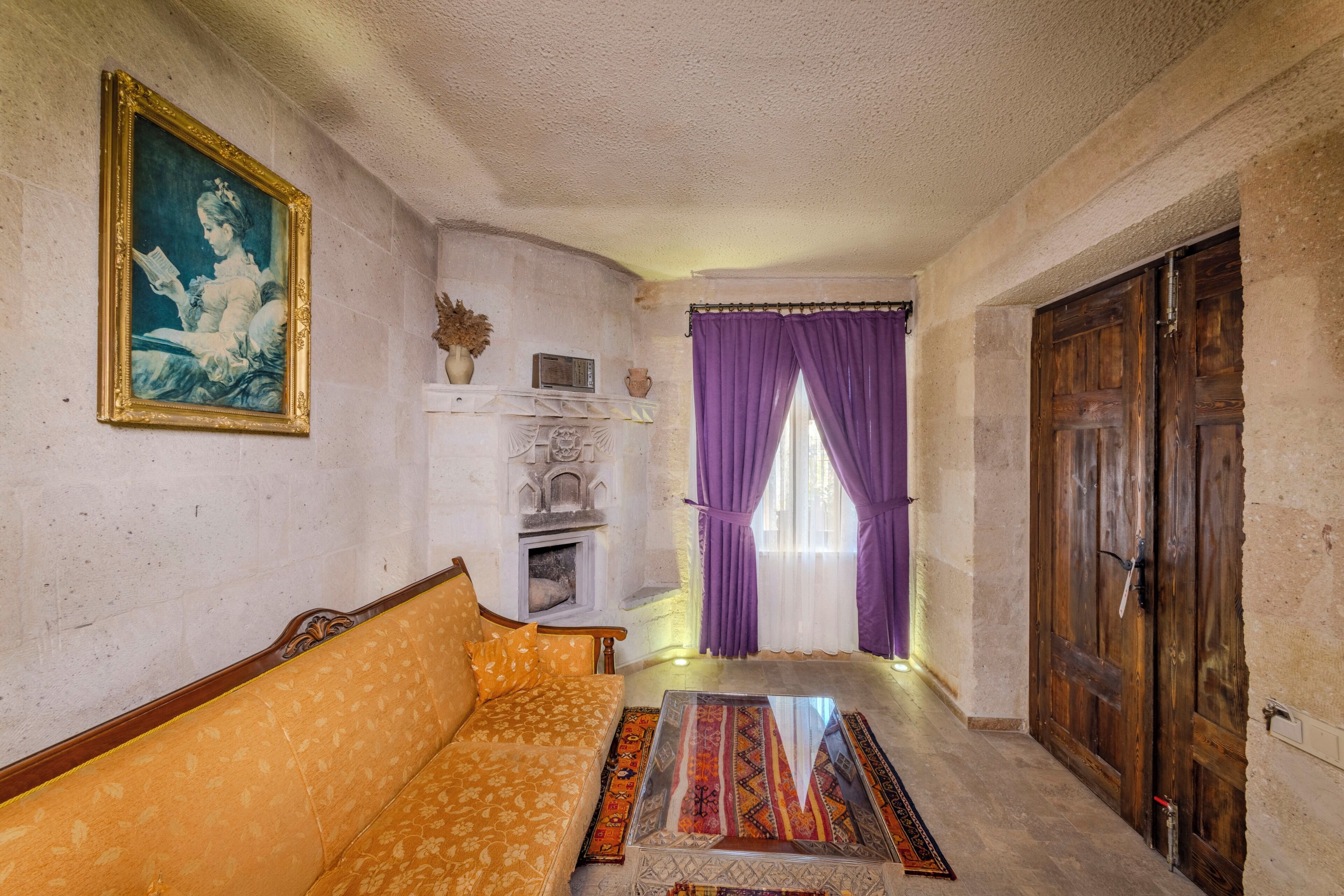 A room with a sofa, a painting, a fireplace, and a wooden door.