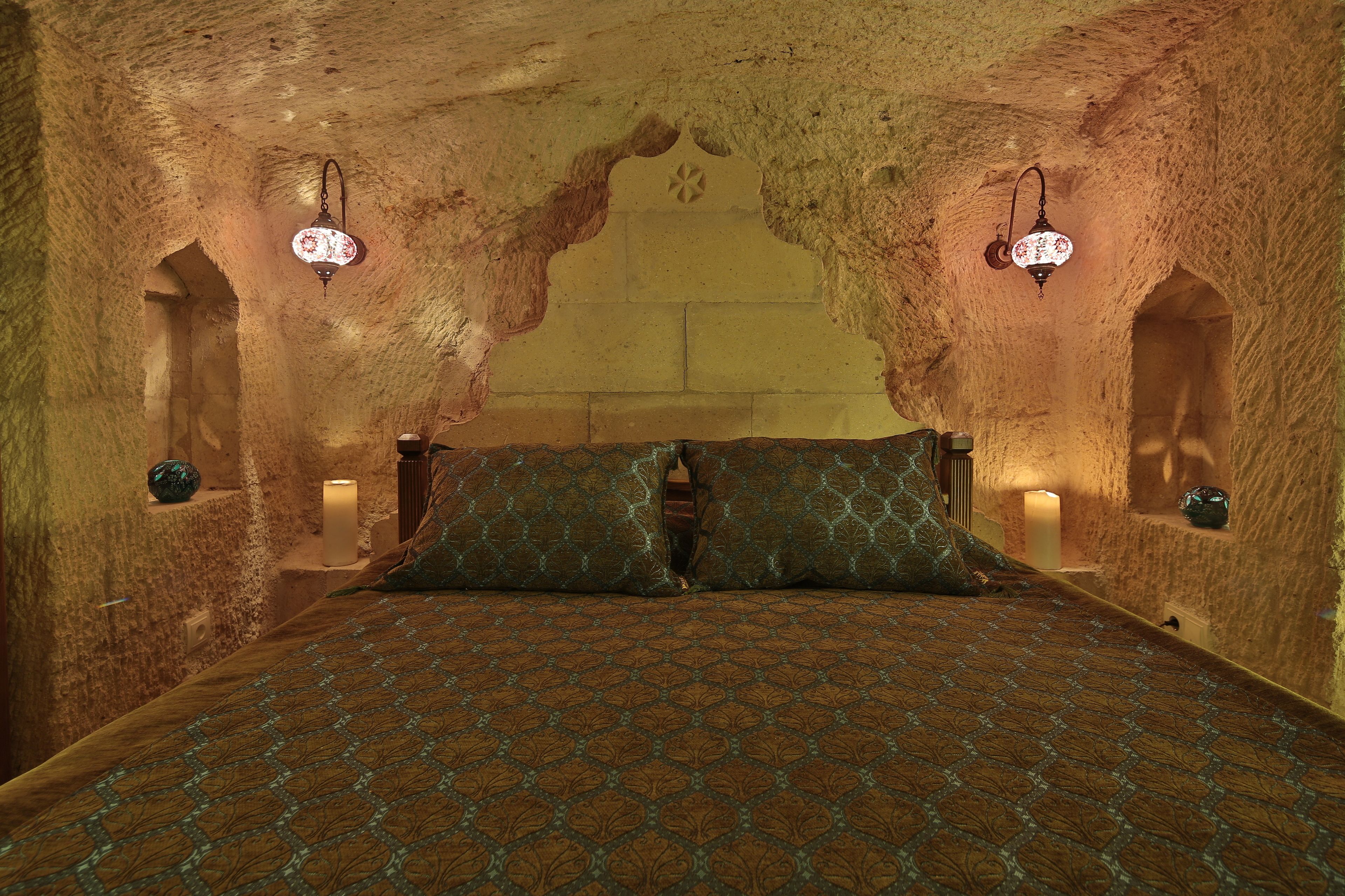 A room with a patterned bedspread, two wall-mounted lamps, and a textured wall.