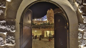 An arched entrance to a building with stone walls and a wooden door. Inside, there are tables and chairs arranged for dining. - Turkish Cave House (Ürgüp)