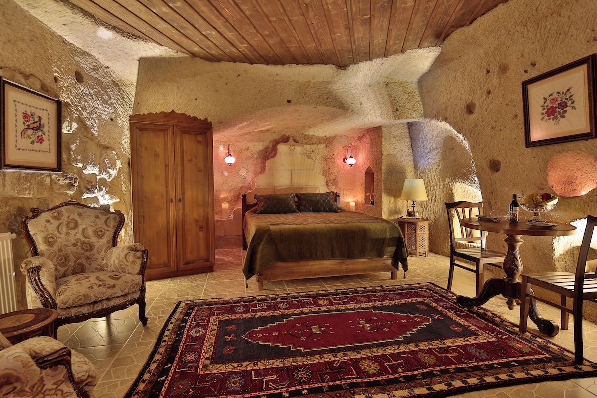 Un dormitorio con techo de madera, una cama con colcha verde, un armario de madera, un sillón estampado floral y una alfombra con diseño.