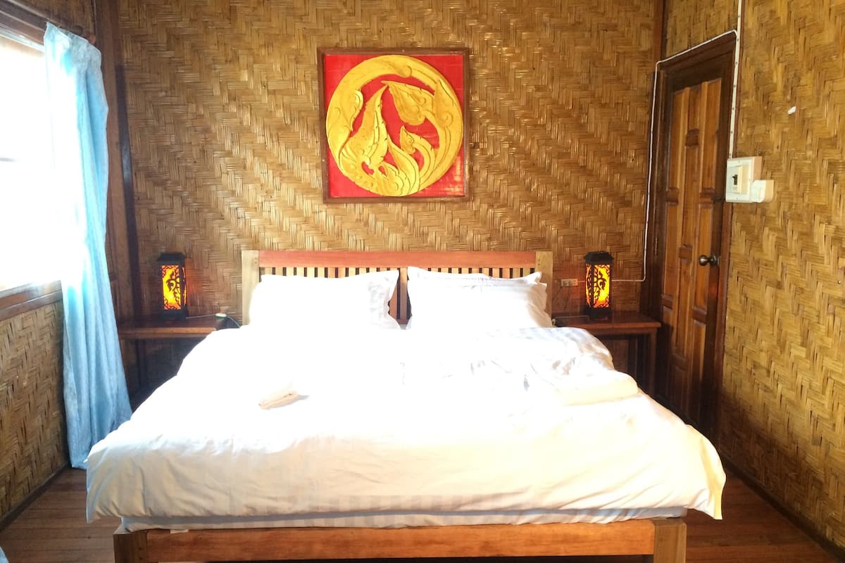 Un lit en bois avec une literie blanche, dans une pièce dont le mur est décoré d’un motif tissé, et au-dessus du lit, on peut voir un emblème rouge et doré.