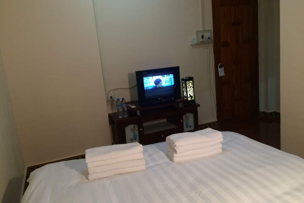 Une chambre d’hôtel avec un lit, un téléviseur posé sur un meuble et une porte visible au fond.