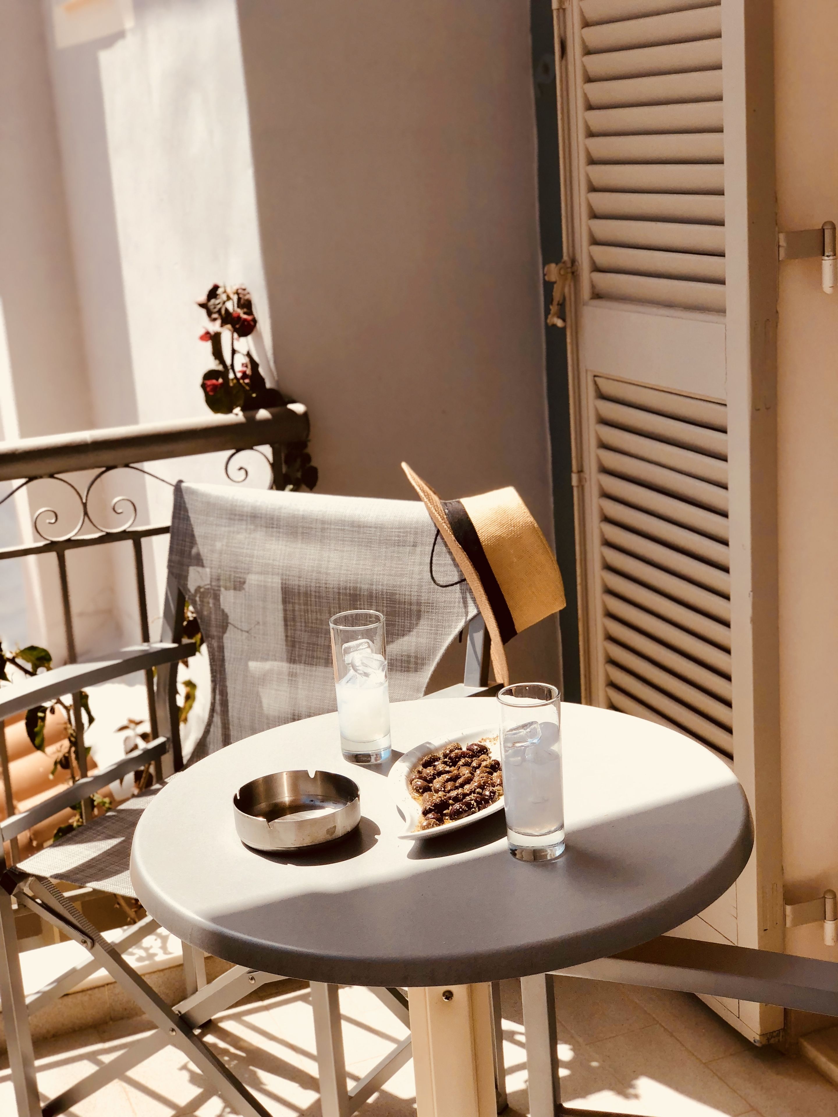 A small round table with a metal bowl, a glass of water, and a plate of food on a balcony.